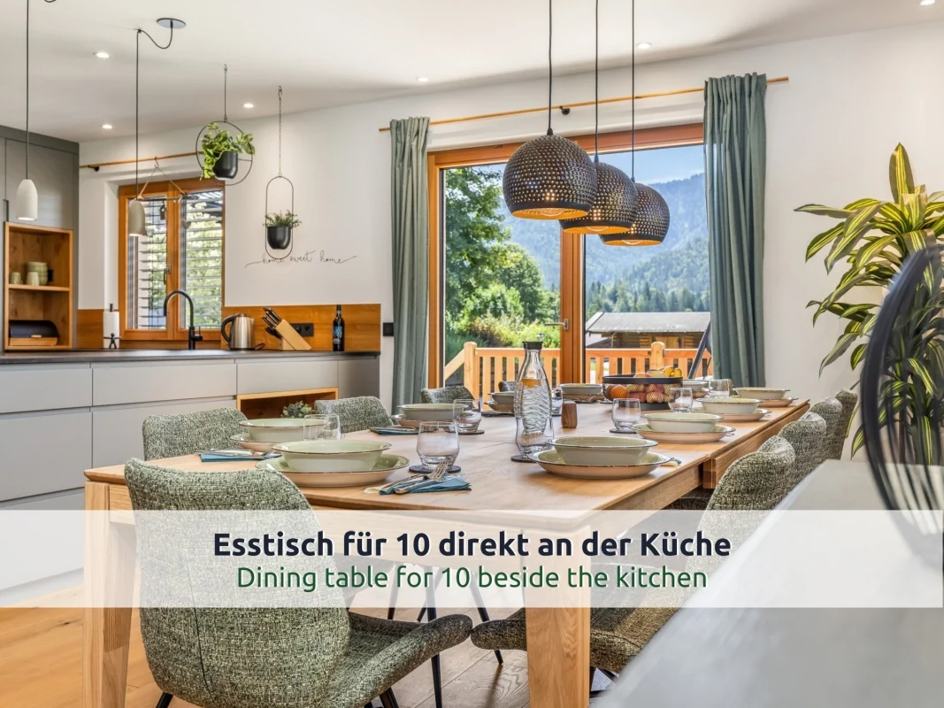 Chalet Reit im Winkl: Esszimmer mit langem Holztisch und grünen Polsterstühlen, gedeckt für viele Gäste, Blick auf Wald und Berge
