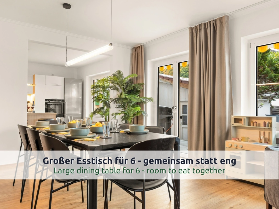 Ferienhaus Ruhpolding: gedeckter Esstisch mit schwarzen Stühlen, daneben eine Spielküche aus Holz, im Hintergrund die offene Küche