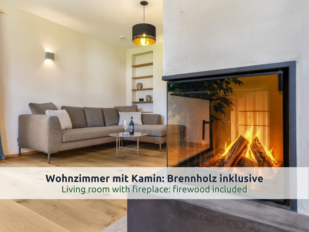 Chalet Reit im Winkl: Wohnzimmer mit grauem Ecksofa, Glastisch und brennendem Kamin hinter Glas