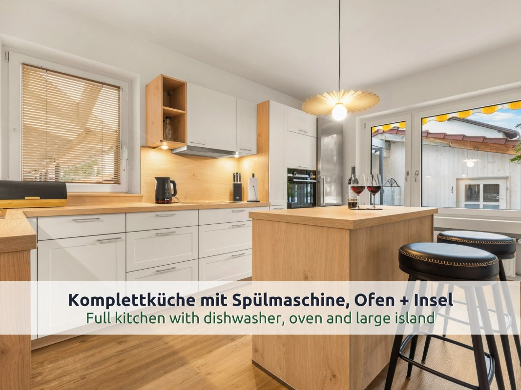 04 Ferienhaus Ruhpolding: helle Küche mit Kochinsel, zwei Barhockern, Backofen und Glastür zur Terrasse