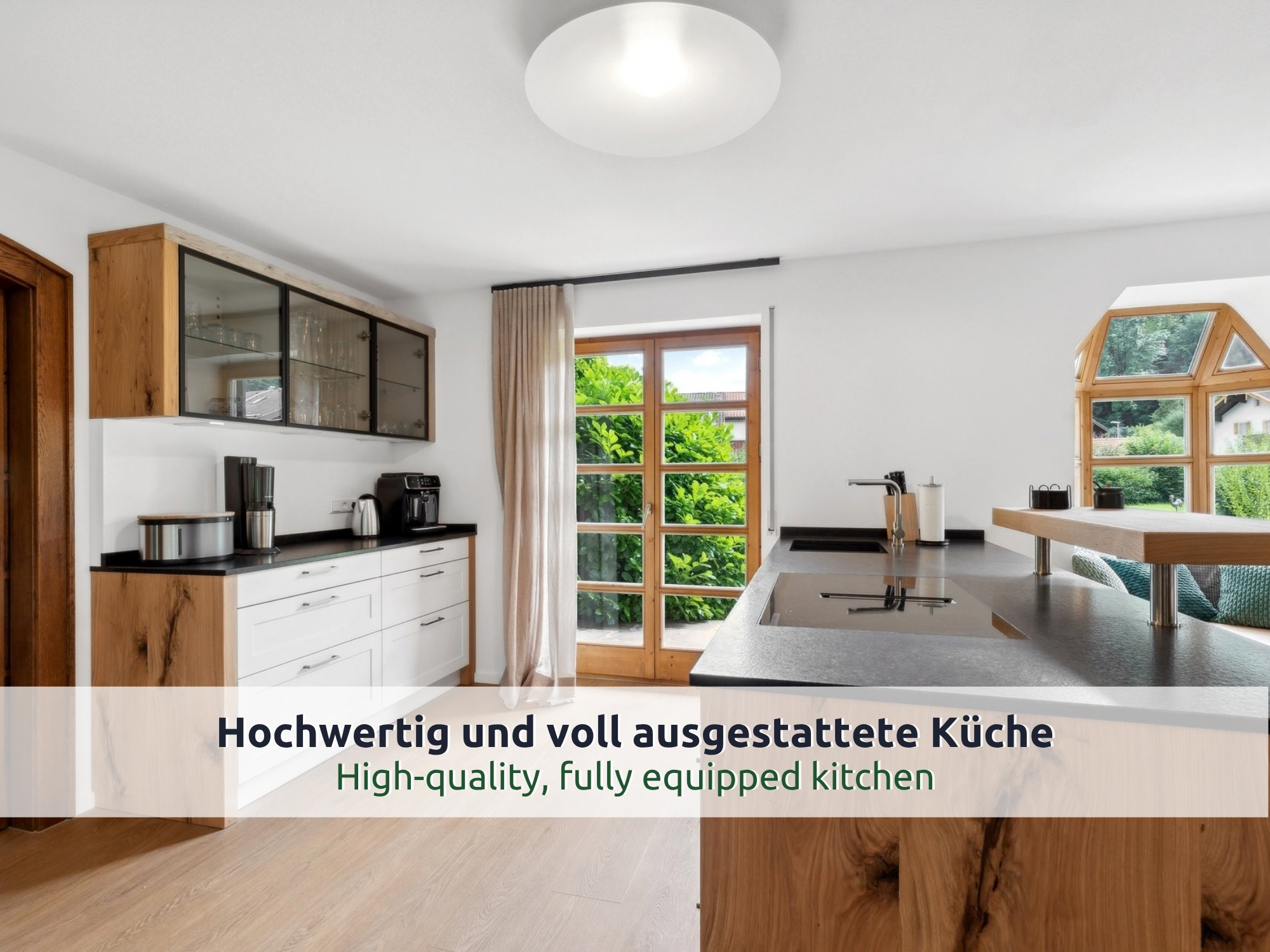 07 Villa Siegsdorf: Küche mit Kochinsel aus Eichenholz, Kochfeld, Hängeschrank mit Glasfronten und Glastür zum Garten