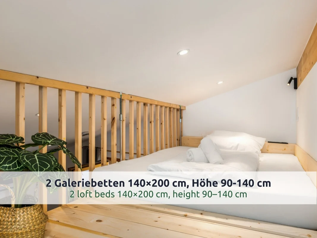 Chalet Reit im Winkl: Galeriebett unter der Dachschräge mit weißer Bettwäsche, Lattengeländer und Leselampe