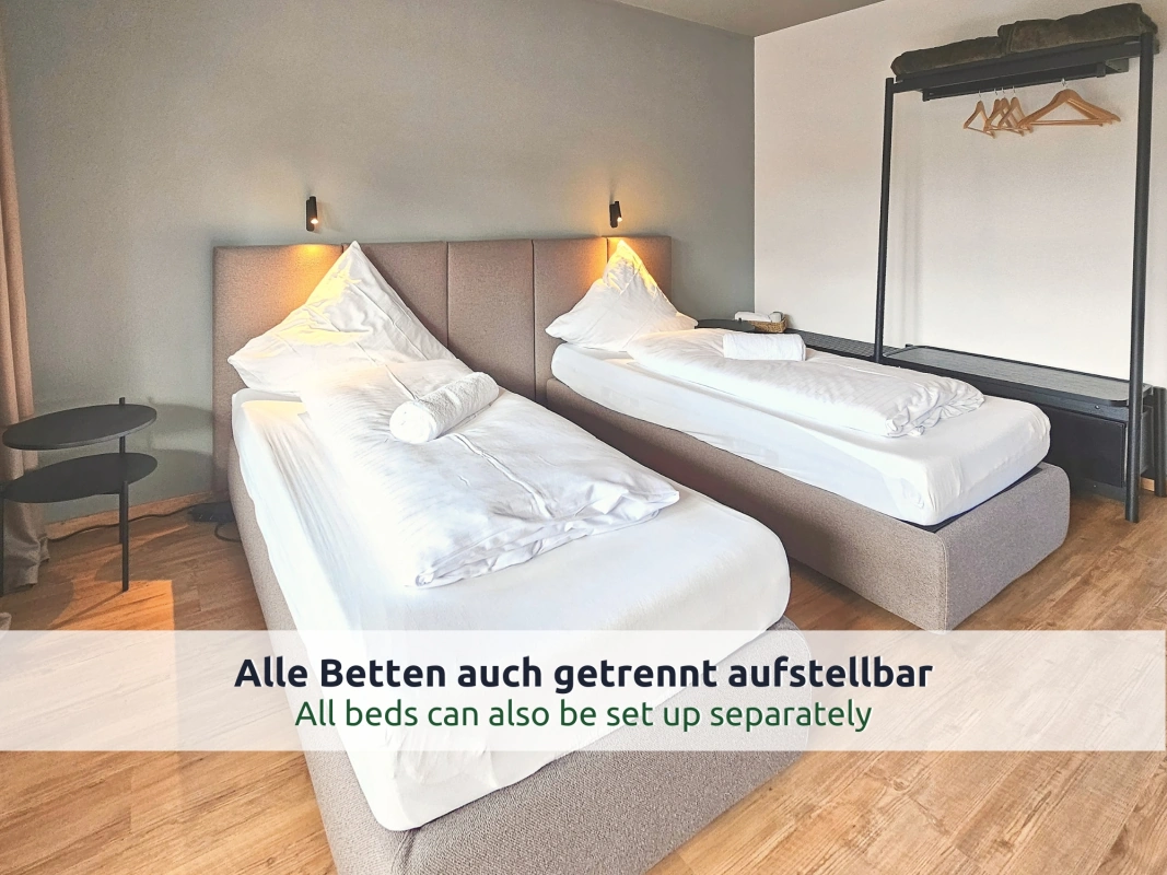 Ferienhaus Ruhpolding: zwei getrennt stehende Einzelbetten mit grauen Polsterbetten, Leselampen und offener Kleiderstange