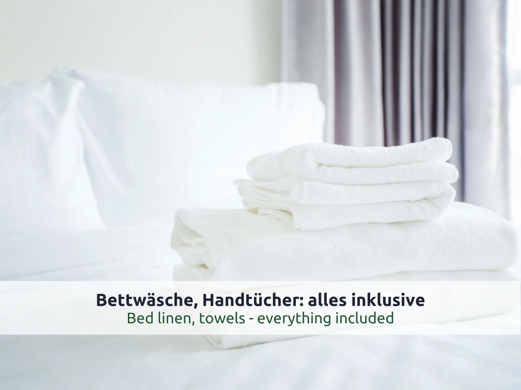 14 Ferienhaus Ruhpolding: gefaltete weiße Handtücher auf einem frisch bezogenen Bett, im Hintergrund ein grauer Vorhang