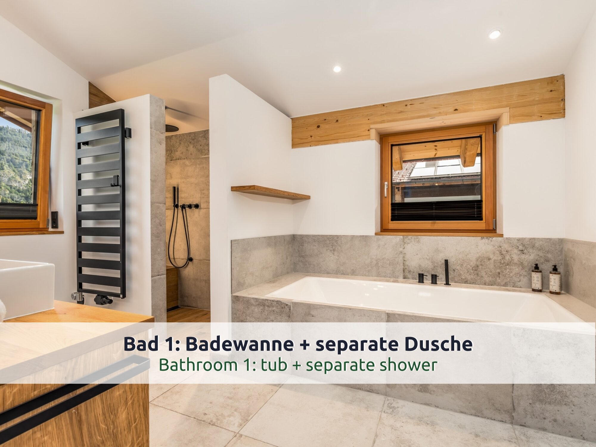Chalet Reit im Winkl: Badezimmer mit Badewanne in Steinoptik, bodengleicher Dusche, schwarzem Handtuchheizkörper, Holzfenster und Aufsatzwaschbecken auf Holz