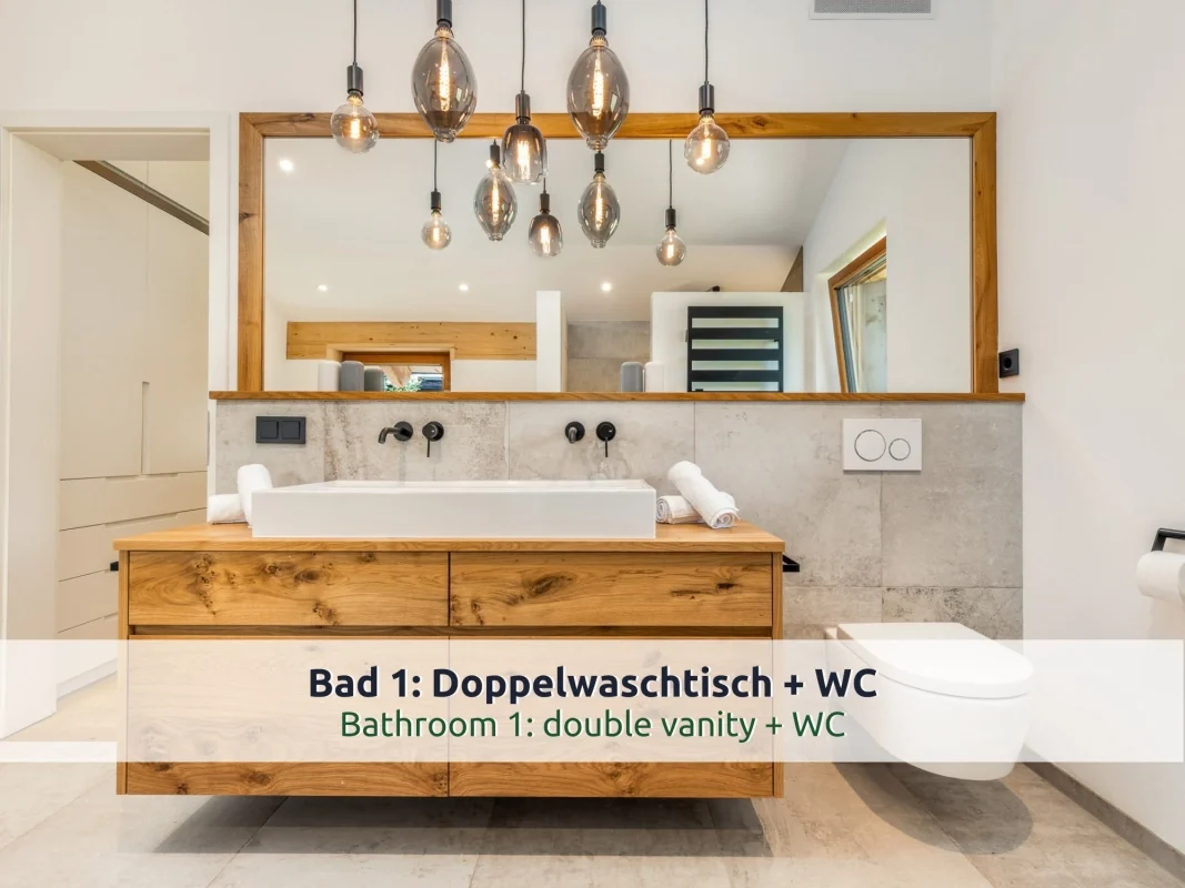 Chalet Reit im Winkl: Waschtisch aus Eichenholz mit Aufsatzbecken, großer Spiegel mit Holzrahmen, Glühbirnen-Pendelleuchten und WC im Bad