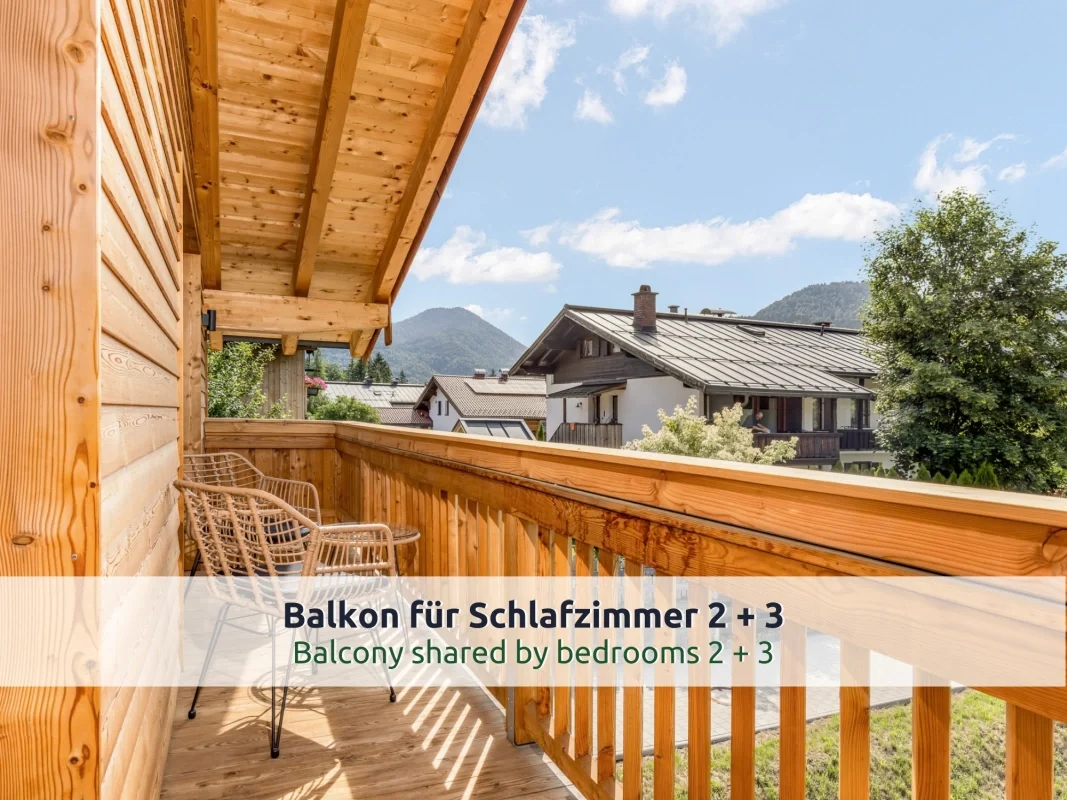 Chalet Reit im Winkl: Holzbalkon im Obergeschoss mit zwei Rattanstühlen und Tischchen, Blick auf Nachbarhäuser und bewaldete Berge