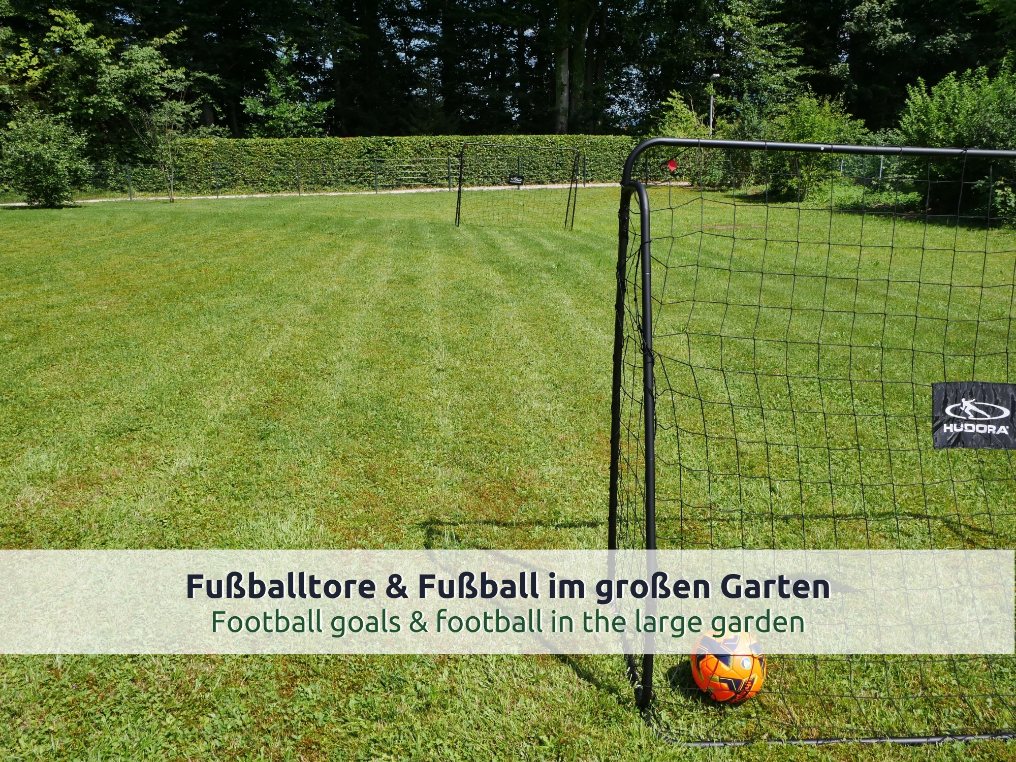 24 Villa Siegsdorf: Fußballtor mit Netz und orangem Ball auf gemähtem Rasen im Garten, dahinter eine Hecke und Bäume