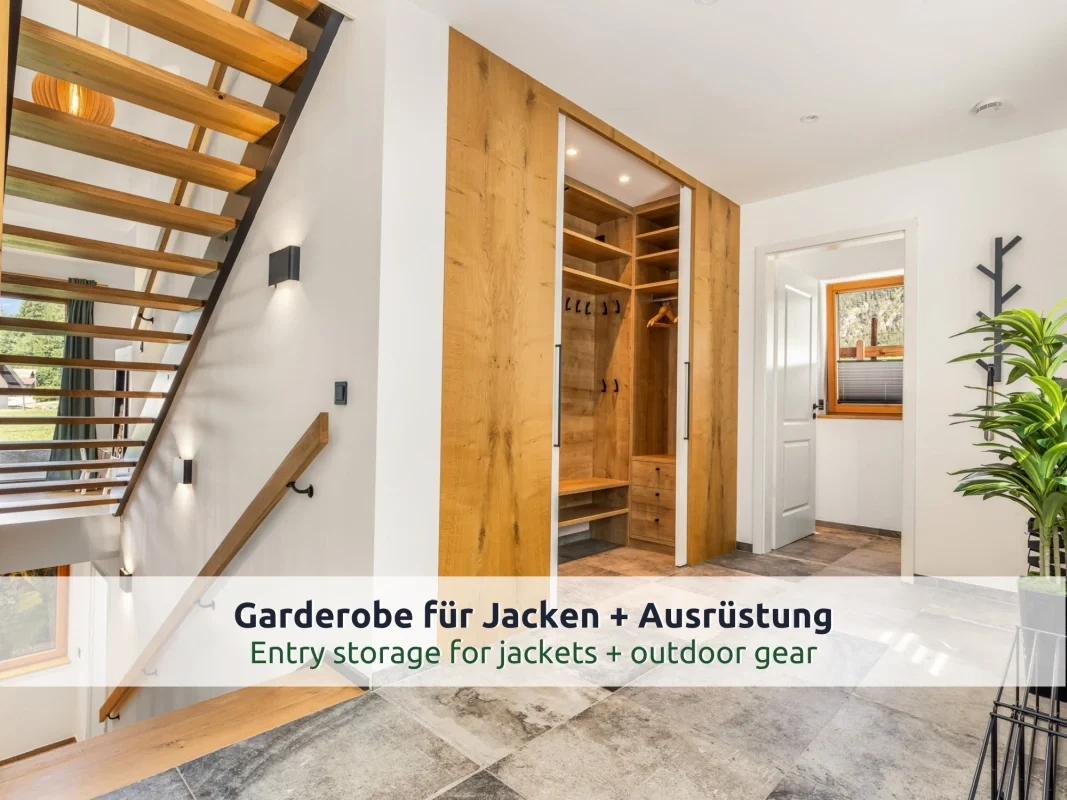 Chalet Reit im Winkl: Eingangsbereich mit offener Holztreppe, Garderobenschrank aus Eiche mit Haken, Steinfliesen, Wandleuchten und weißer Tür