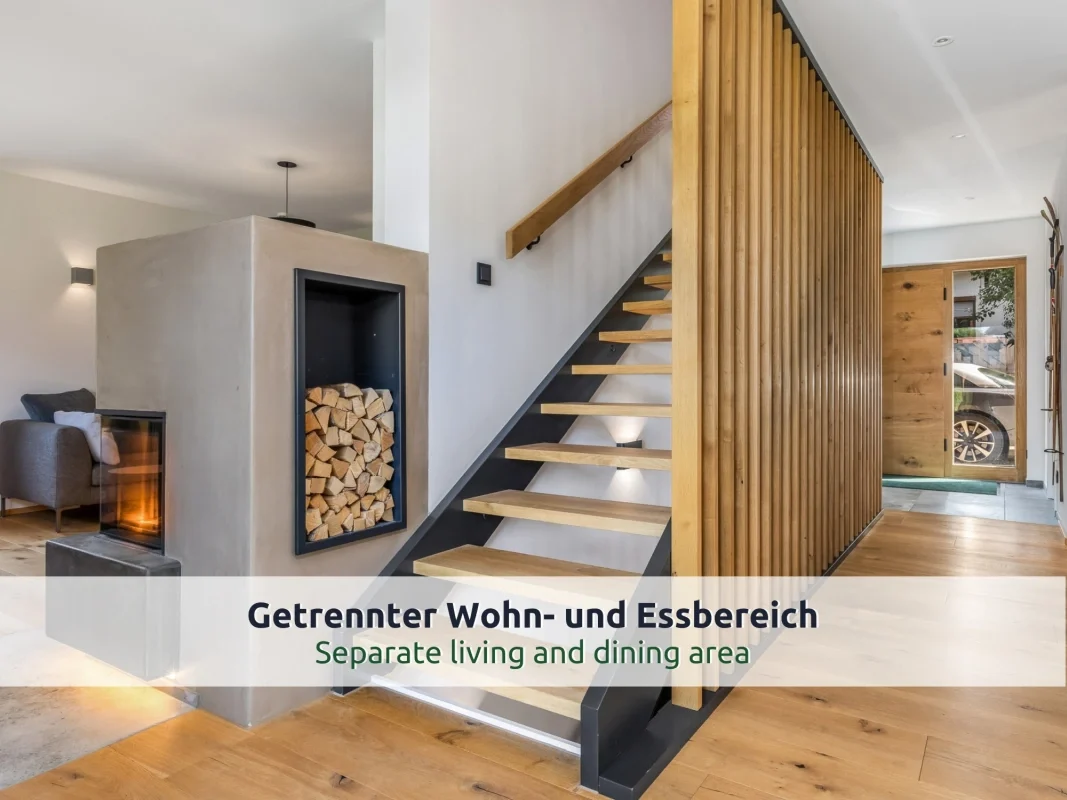 Chalet Reit im Winkl: offene Treppe mit Holzstufen und Lattenwand, daneben ein Kamin mit Holzfach und die Haustür aus Holz und Glas