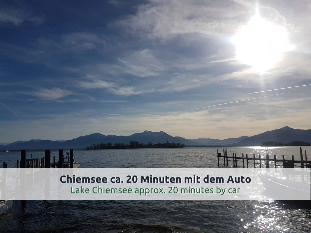 Ausflugsziel Chiemsee: Holzstege, Boote und eine Insel im Gegenlicht vor den Bergen