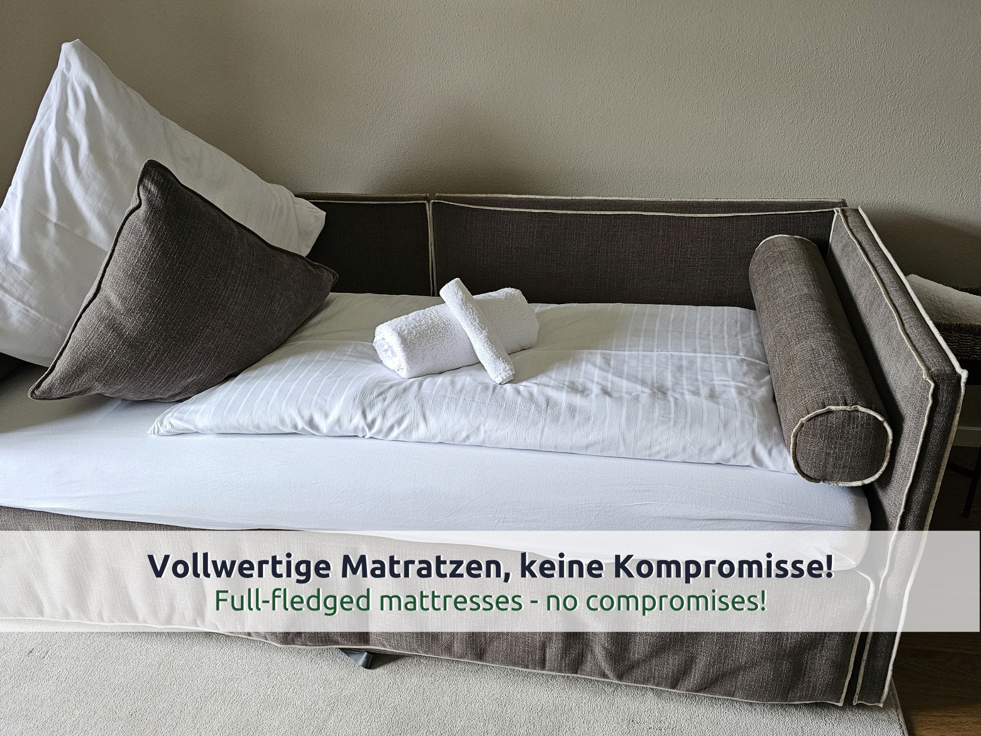38 Villa Siegsdorf: ausgezogenes graues Bettsofa mit weißer Bettwäsche, Kissen, Nackenrolle und gerollten Handtüchern