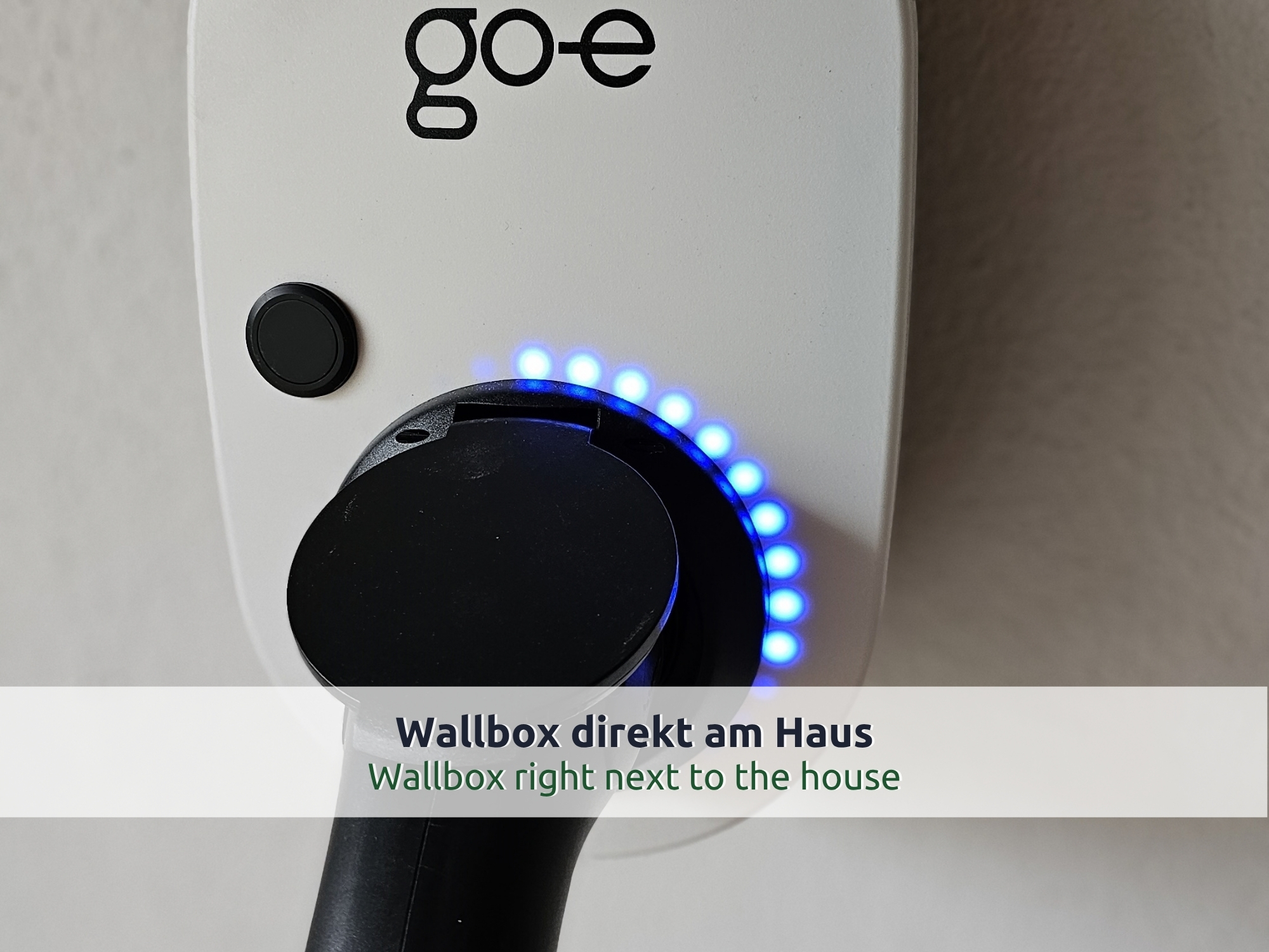 52 Villa Siegsdorf: Wallbox mit blau leuchtendem Ring und eingestecktem Ladekabel an der Hauswand